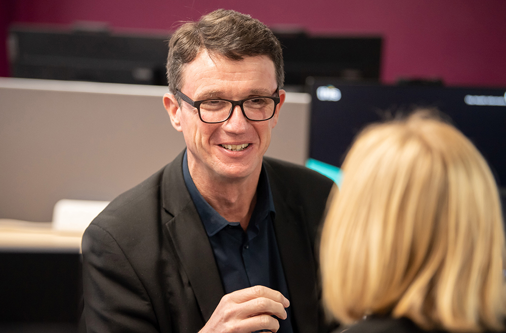 Julian smiling talking to another colleague in the Elland office.