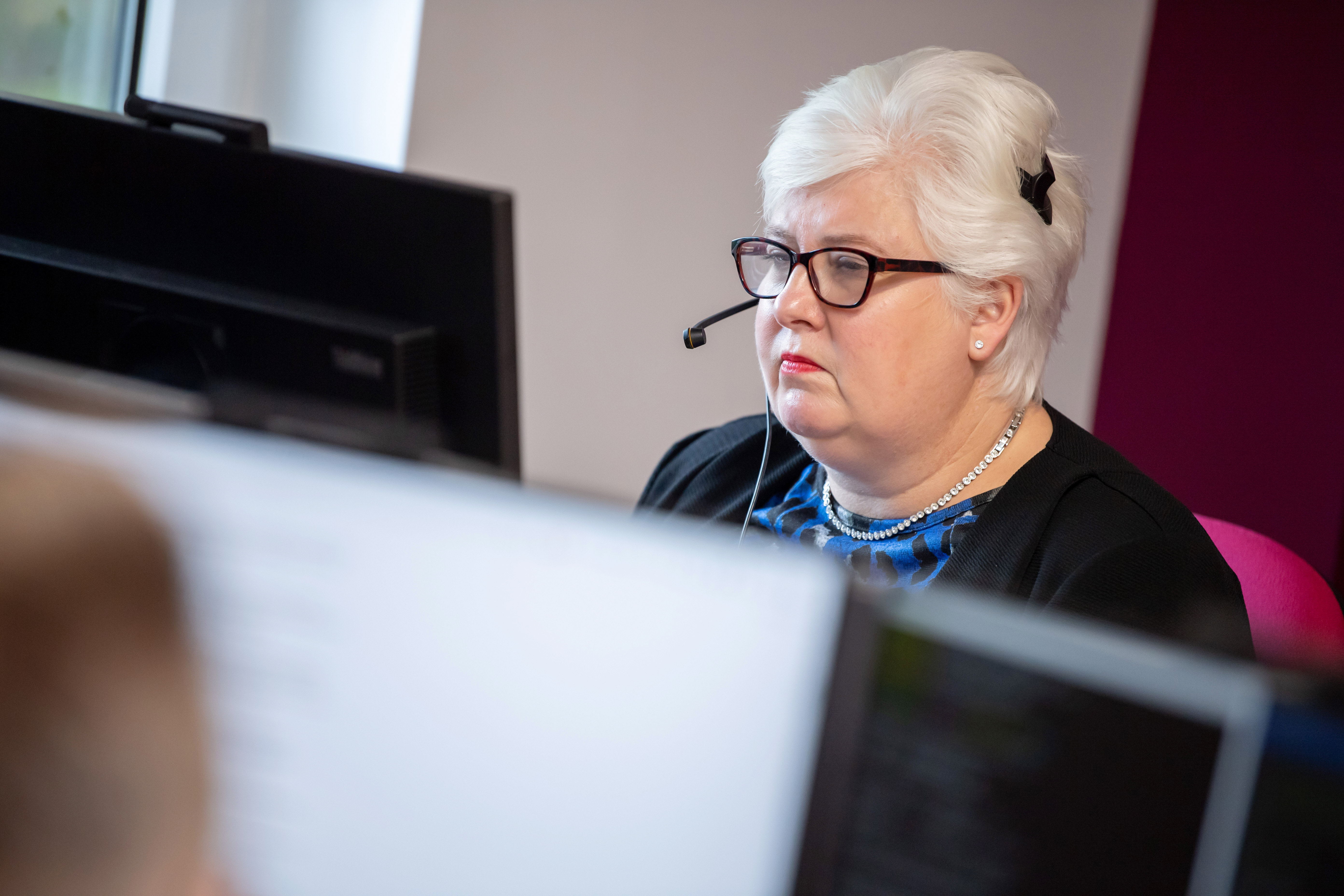 Female colleague wearing glasses with a headset on looking at her computer screen.