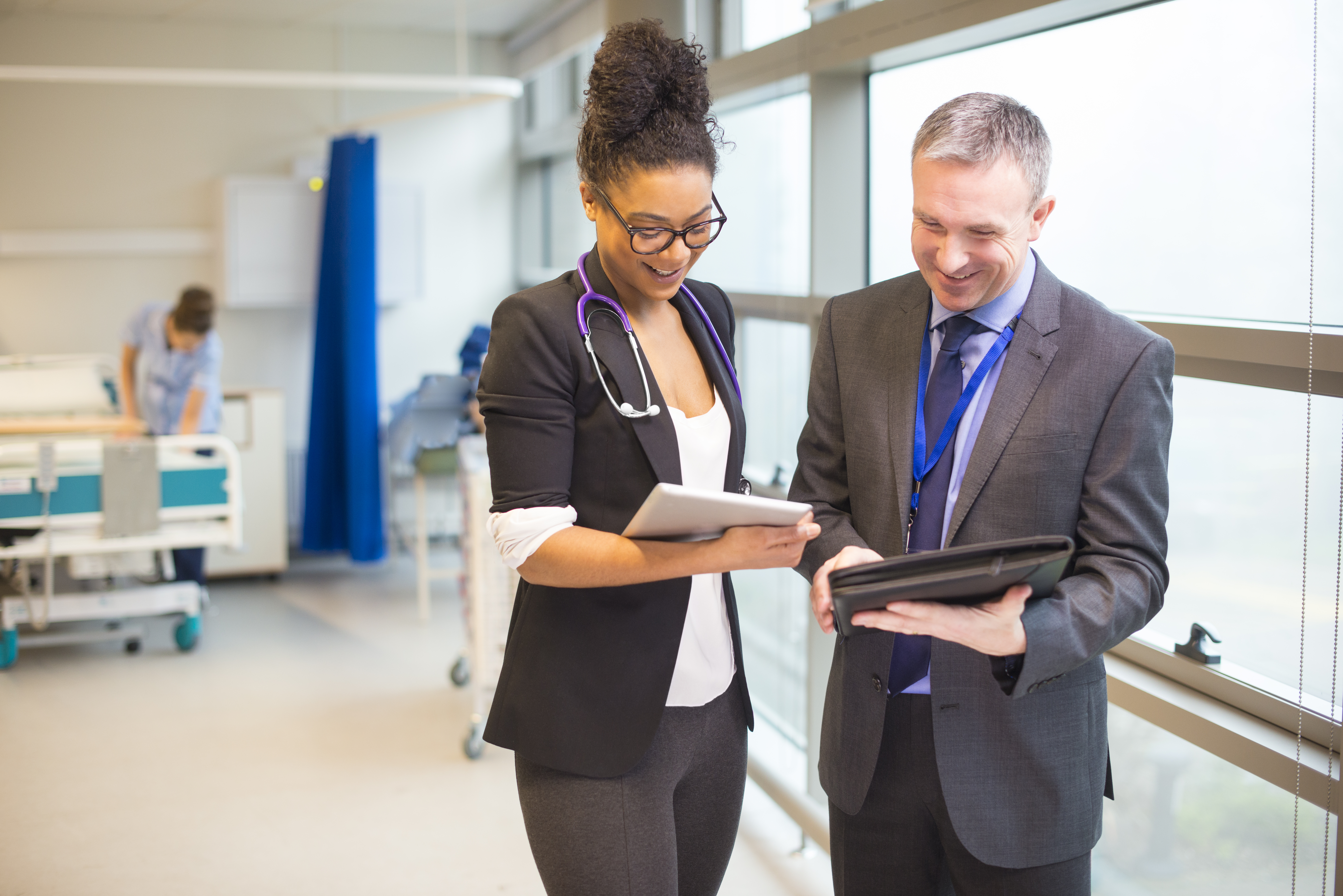 Two colleagues inside a hospital ward looking at an tablet screen.